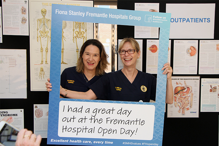 Two female nurses stand in front of a cut-out frame that reads 'I had a great day at the Fremantle Hospital Open Day'